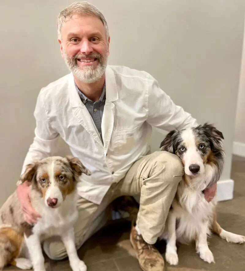 Our pharmacist kneeling with his two Australian Shepherd dogs